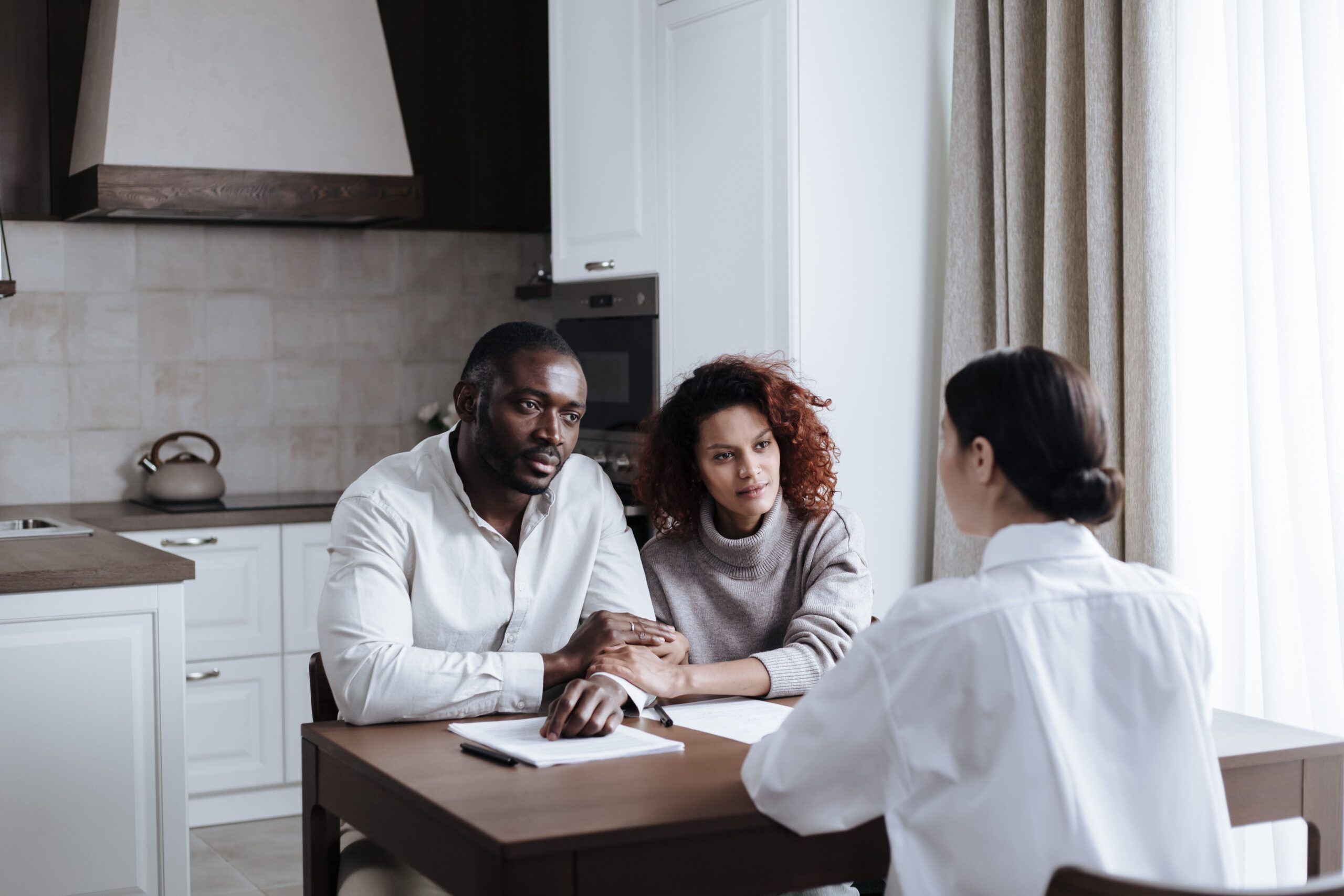 A couple discusses adoption with a social worker in a modern kitchen setting.